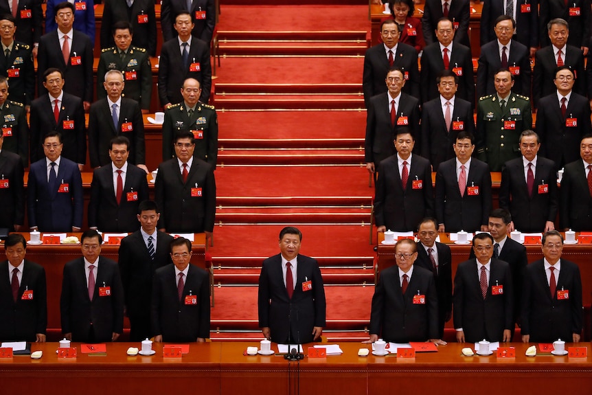 Members of the Chinese Communist Party stand in a hall with red carpet. 