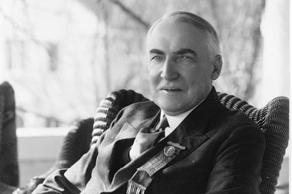 Warren Harding a suit, leaning back on a cane armchair on a porch