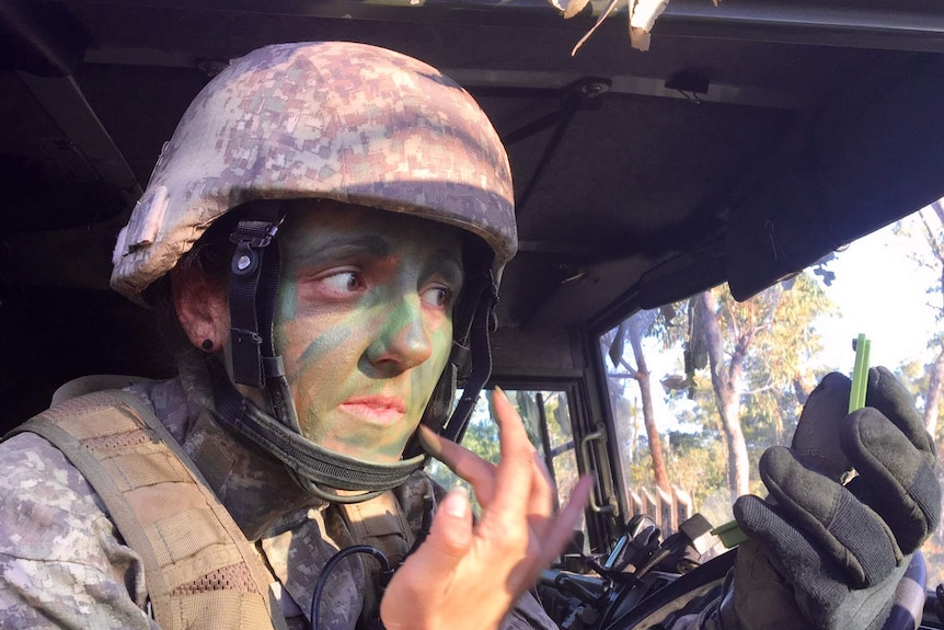 A New Zealand soldier uses a compact mirror in a vehicle to apply camouflage paint to her face