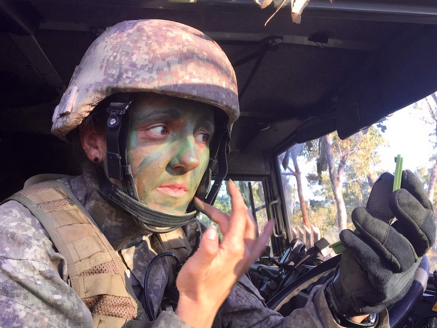 A New Zealand soldier uses a compact mirror in a vehicle to apply camouflage paint to her face