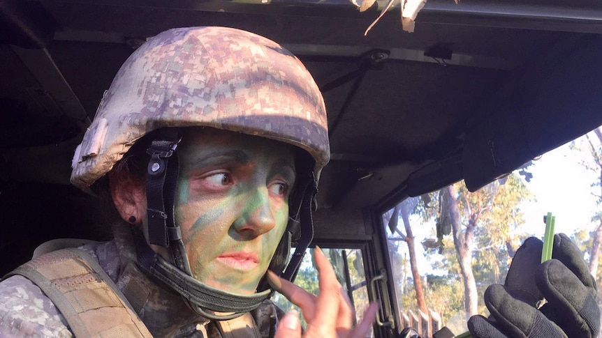 A New Zealand soldier uses a compact mirror in a vehicle to apply camouflage paint to her face