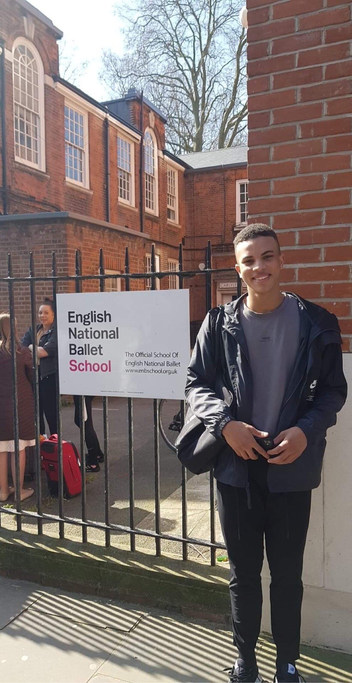 A young man stands in front of a sign reading 'English National Ballet School'