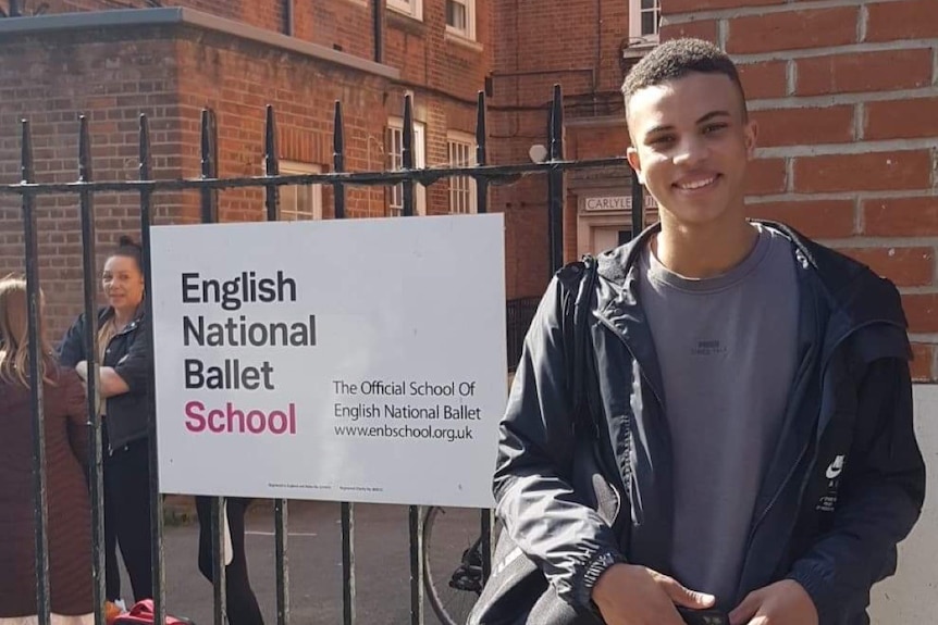 A young man stands in front of a sign reading 'English National Ballet School'