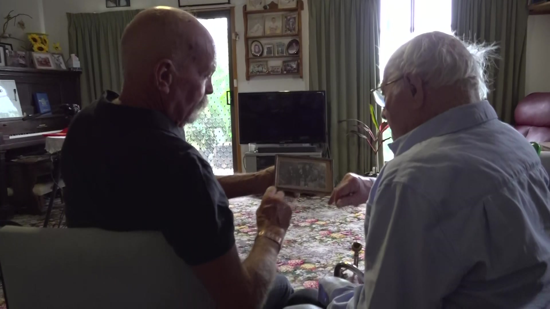 Middle aged man and elderly gentleman looking at a framed photo together in a lounge room