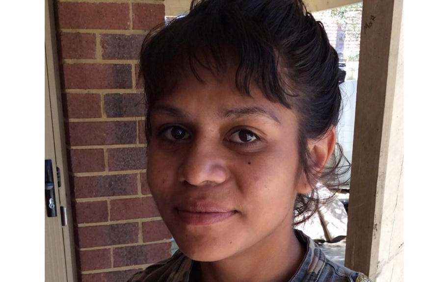 A young woman stands near a brick wall smiling at the camera