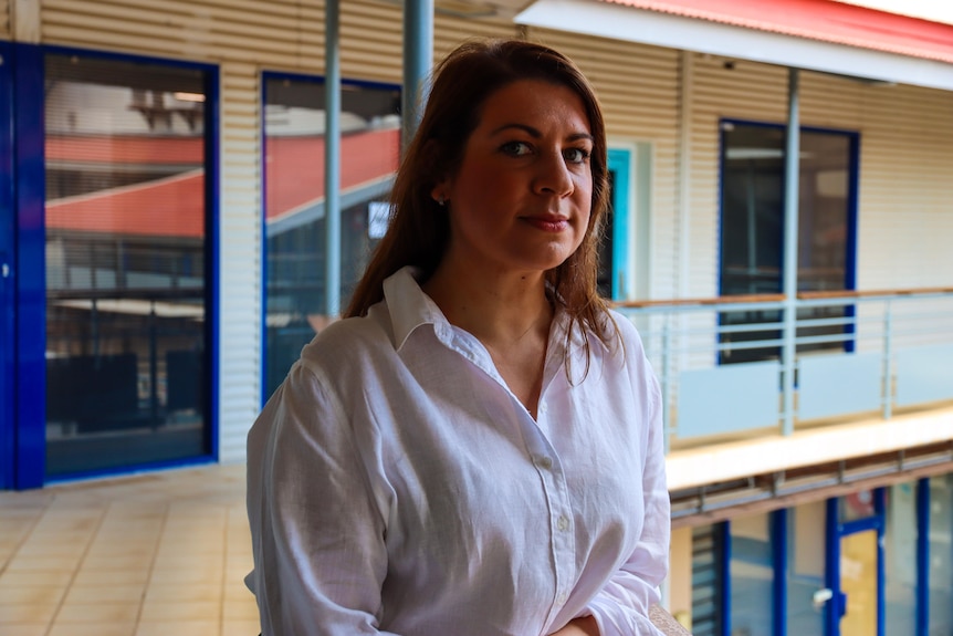 A woman in a white shirt looks at the camera. 