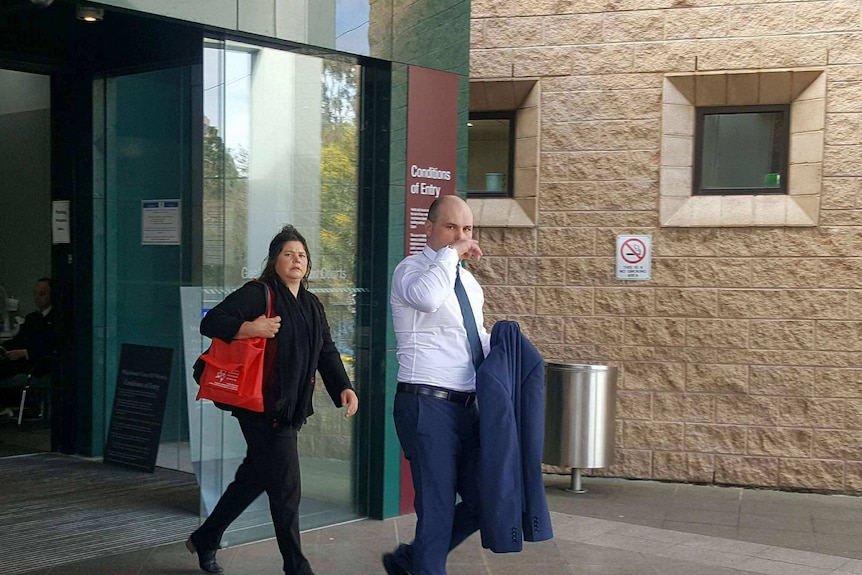 Scott Hammond wearing a suit walks out of a courthouse, partially covering his face with his hand