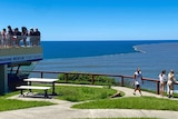 People overlooking the ocean and the water closest to shore is brown while water further out is blue