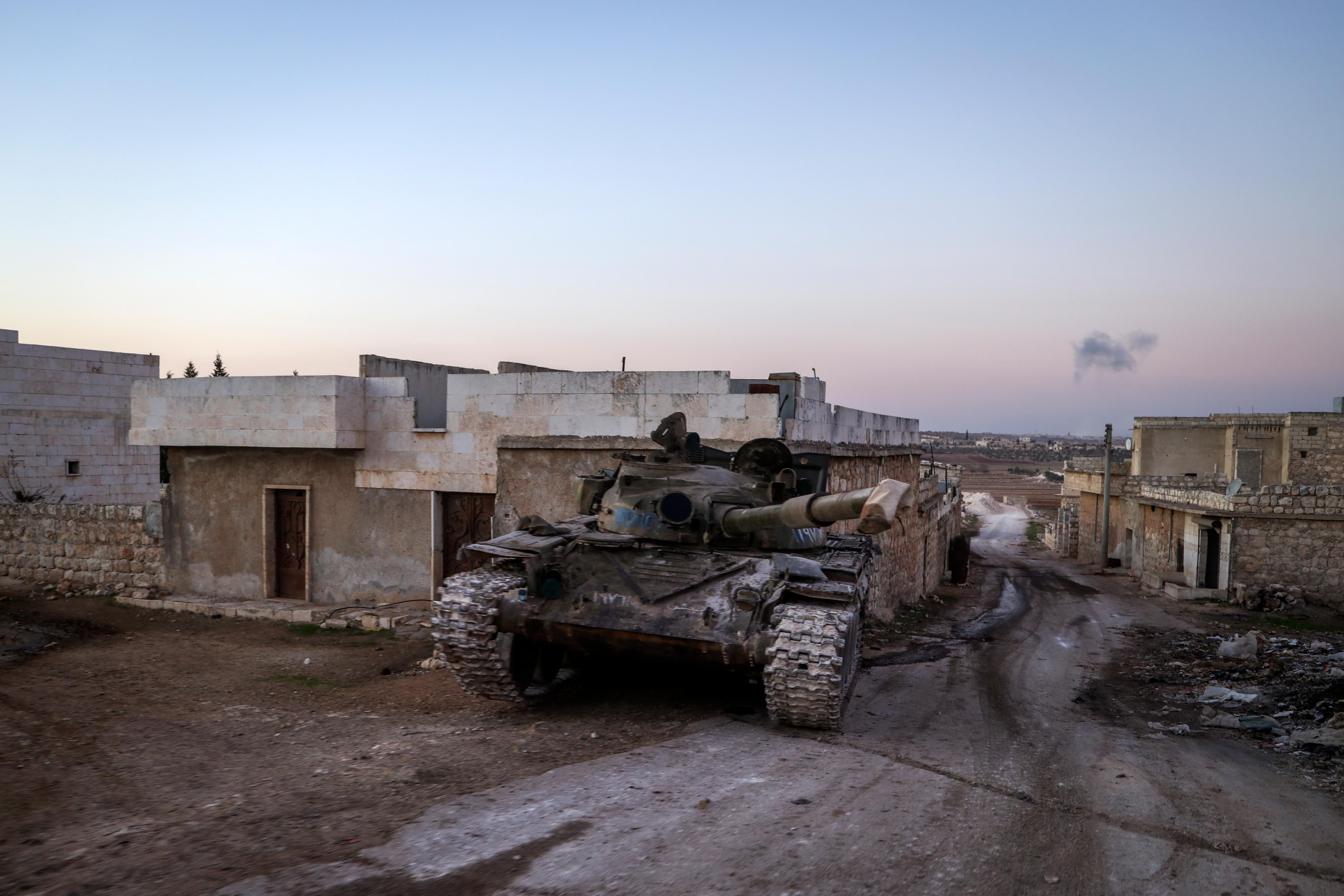 A destroyed tank lies on a dusty roadway.