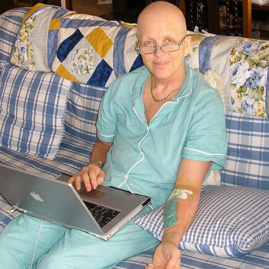 A woman without hair in a hospital gown sitting and smiling at the camera.
