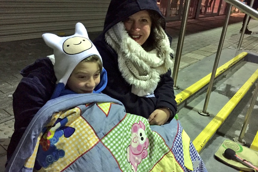 A mother and son all rugged up with beanies and scarves under a quilt at Mount Lofty