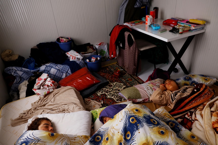 People lay on the ground covered in blankets inside a small room. 