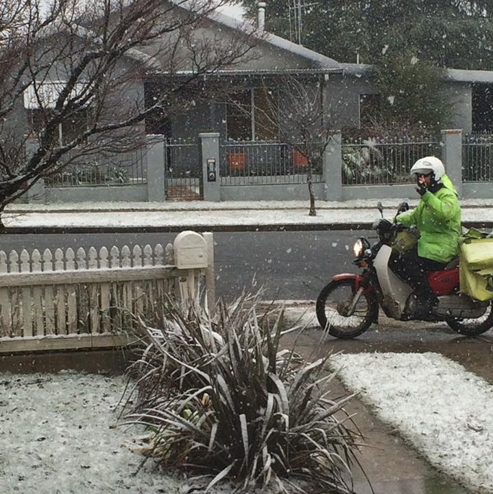 A postal officer on a motorbike delivers mail in the snow on a residential street in Orange