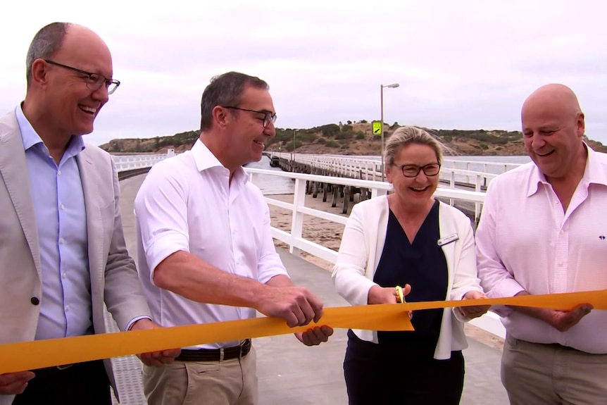 Four people overlook the cutting of a ribbon on a causeway