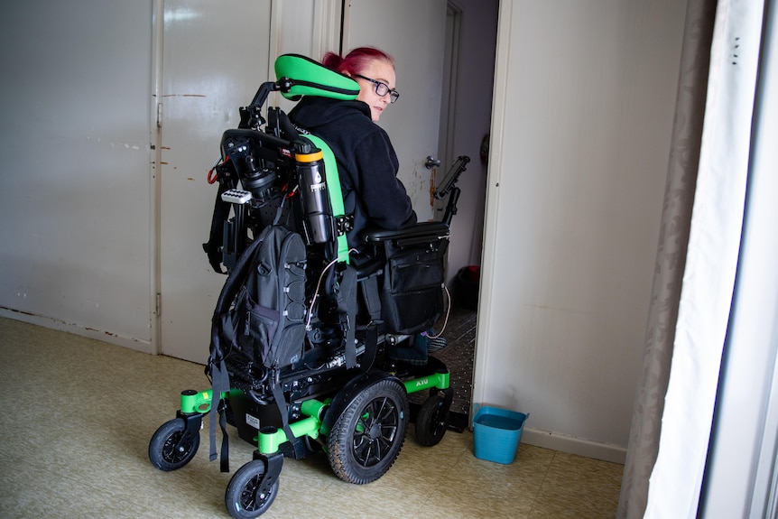 A woman tries to navigate her wheelchaiur through a narrow internal door frame.