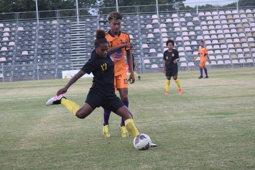 A PNG women's national football team member kicks a ball during a friendly match with men.