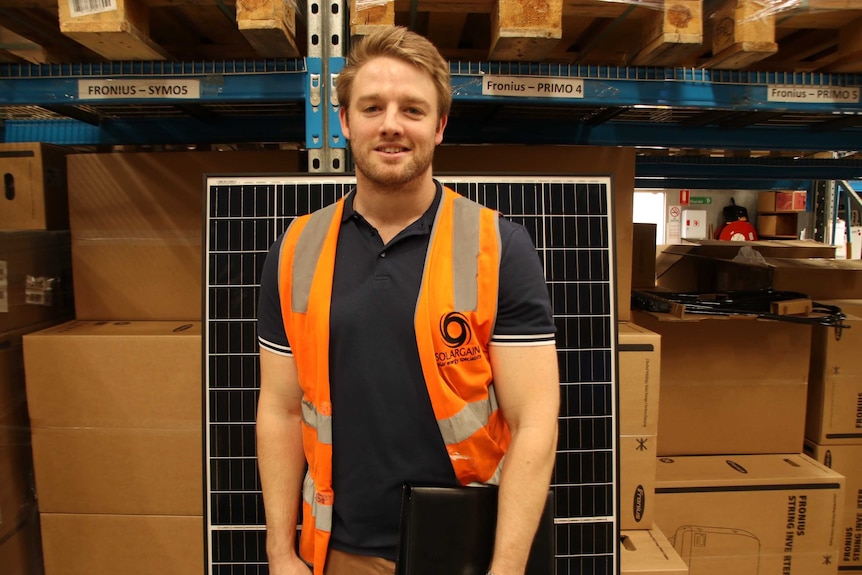 A man in a high-viz vest stands in a store room in front of racks of products on shelves.