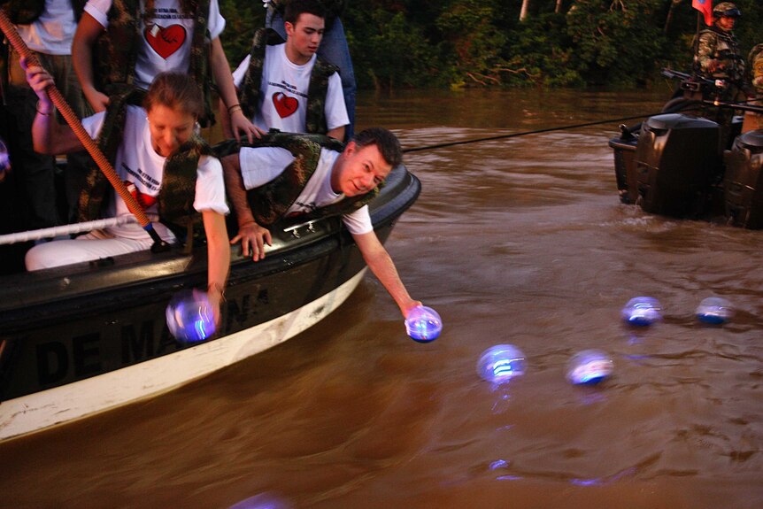 Photo of a man with others in a raft putting a glowing indigo ball into the river