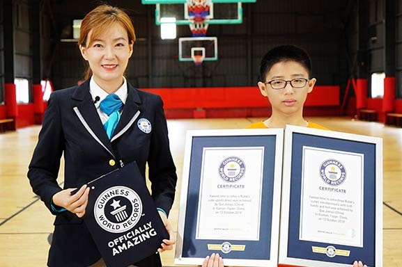 Que Jianyu holds two Guinness World Records certificates while an official adjudicator stands next to him.