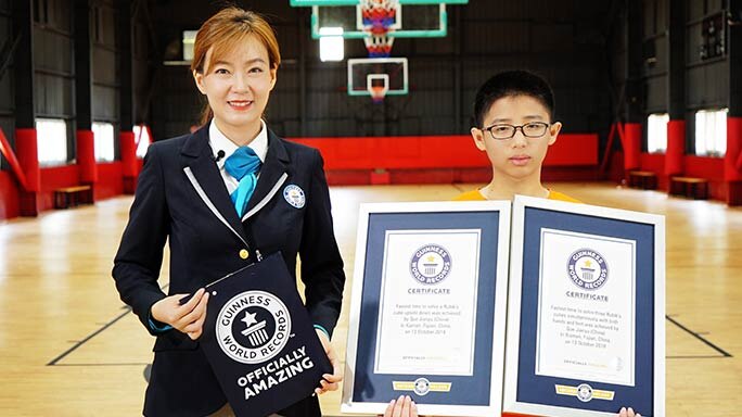 Que Jianyu holds two Guinness World Records certificates while an official adjudicator stands next to him.