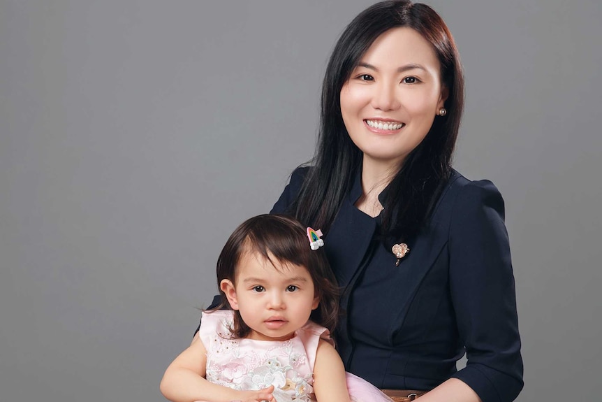 A woman poses for a portrait while holing a young girl on her lap.