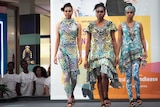 Three female Indigenous models walk in synchronisation down a catwalk.