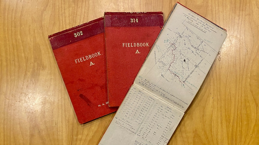 two red notebooks and one notebook opened on a page with a map drawing