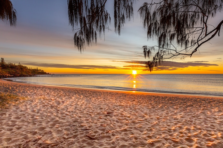 A sun ruses over the water in front of a beach.