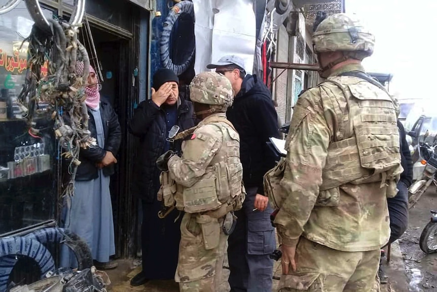 Two US soldiers in uniform speak to shop owners in the town of Manbij, Syria