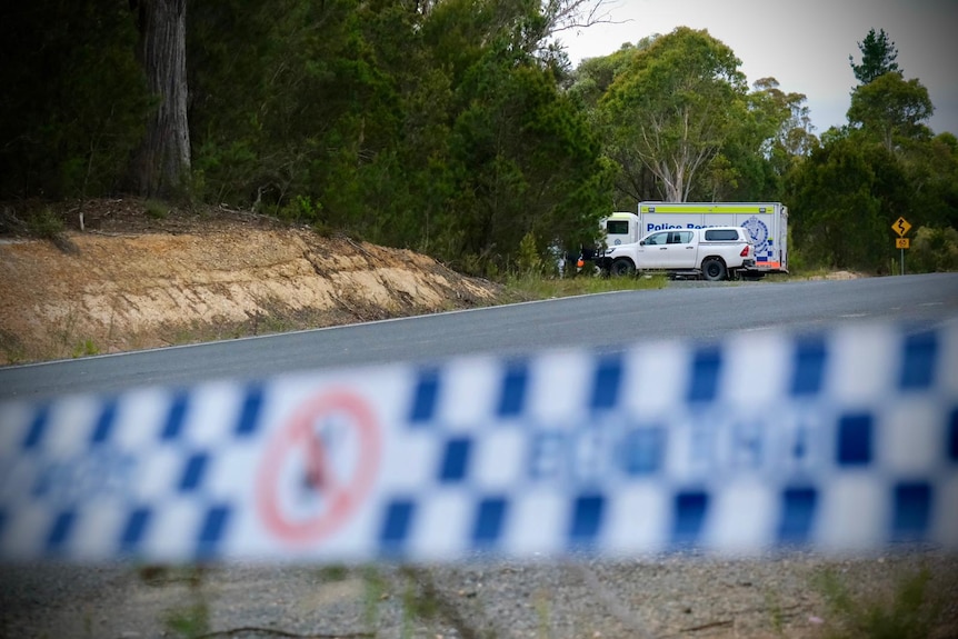 A police rescue vehicle and white car seen alongside a rural road as police tape crosses the foreground.