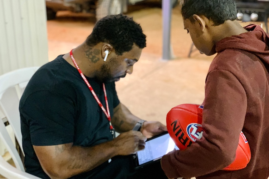 A man with dark hair and tatoos consults a clipboard as a young child watches on