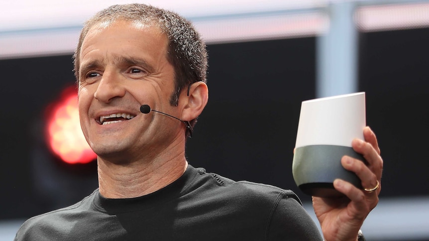 A man in a black T-shirt holds up a small electronic device.