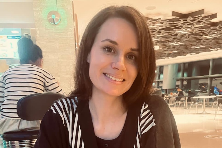 A woman with brown hair smiles in a airport lounge.