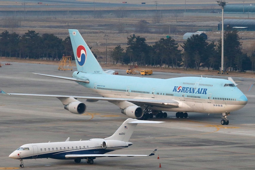 A blue and white commercial aeroplane taxis along the runway with other aircraft around it.