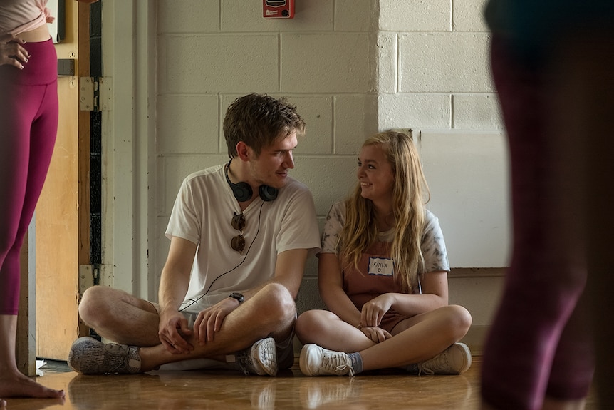 Colour still of director Bo Burnham sitting crossed legged next to Elsie Fisher on the set of Eighth Grade.