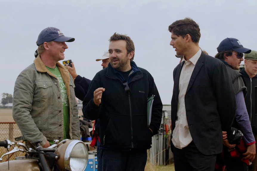 Richard Roxburgh, Robert Connolly and Eric Bana talk on the set of Romulus, My Father surrounded by crew members and film gear.