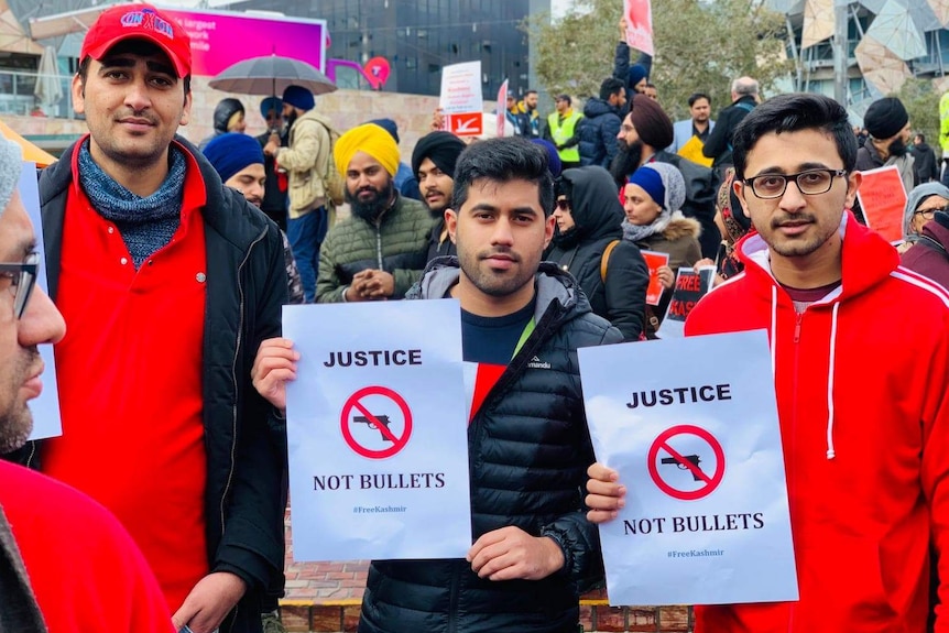 Three men hold small posters in support of Kashmir's autonomy