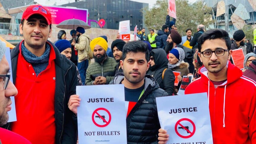 Three men hold small posters in support of Kashmir's autonomy