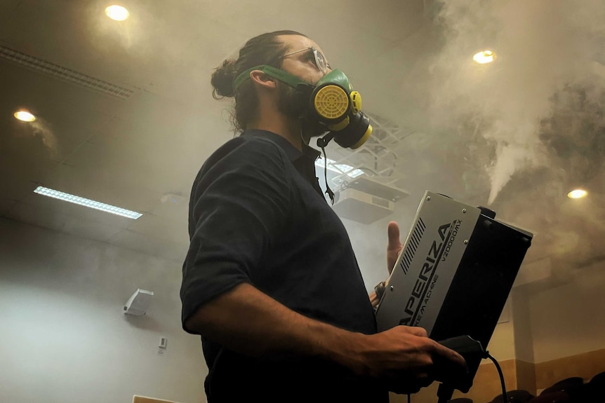 A man holding a smoke machine looks up at the ceiling in an enclosed room.