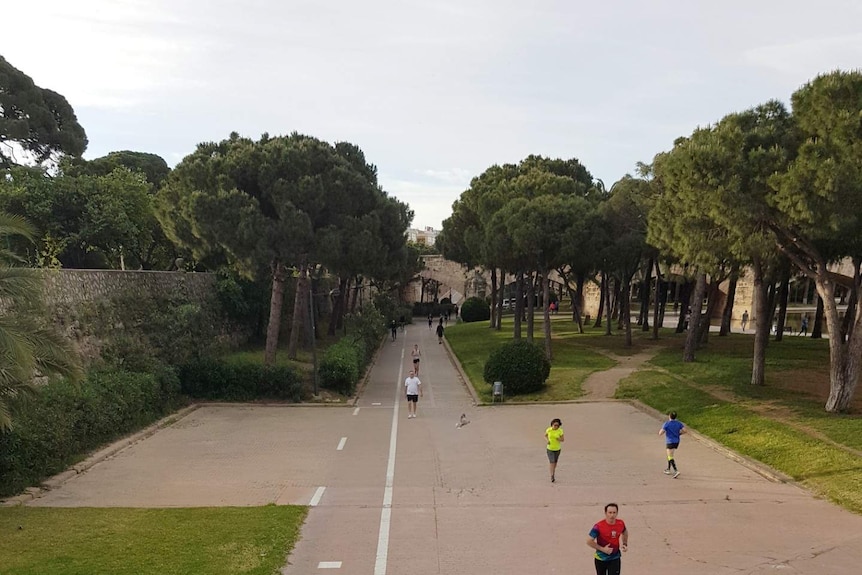 About 10 runners jog through a small section of park