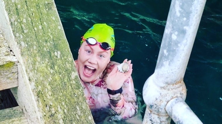 Canberran Ashleigh Webb in the water near a jetty, looking up and smiling at the camera.