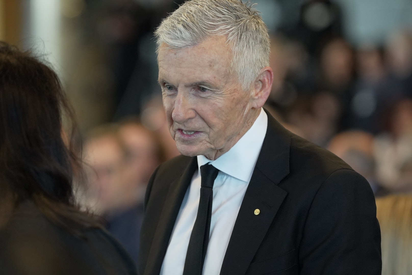 Bruce McAvaney sorri enquanto conversa com alguém. 