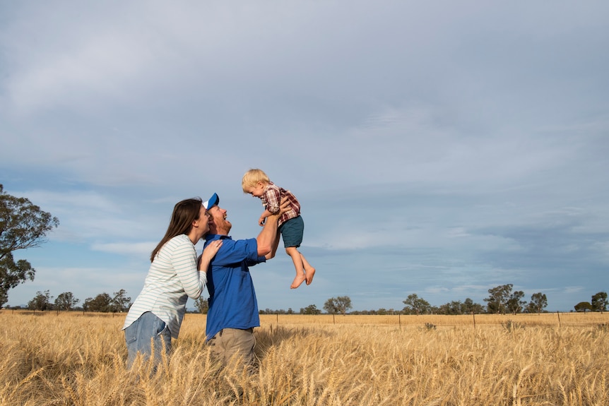man, woman and child in a field of wheat with blue sky and clouds above
