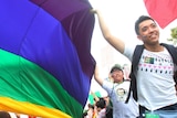 Parade participants walk through a Taiwan street carrying a billowing rainbow flag signifying LGBTIQ rights