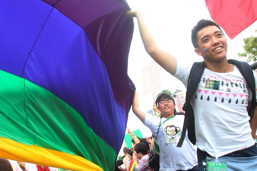 Parade participants walk through a Taiwan street carrying a billowing rainbow flag signifying LGBTIQ rights