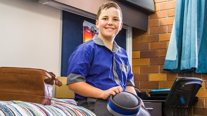 School boy sitting on a bed in a boarding school.