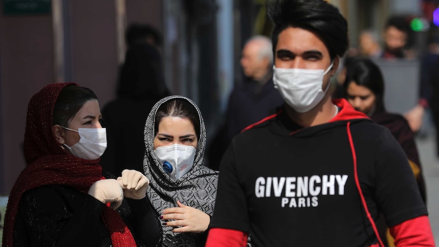 Pedestrians wear masks as they walk down a busy street.