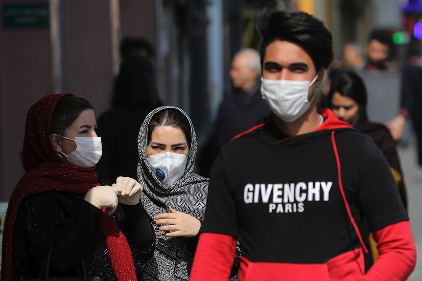 Pedestrians wear masks as they walk down a busy street.