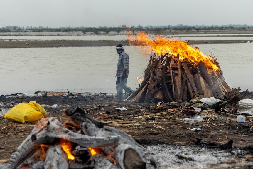 한 남자가 갠지스 강 유역에서 코로나 바이러스 (Covid-19)로 사망 한 사람들과 함께 불타는 소각로를지나갑니다. 