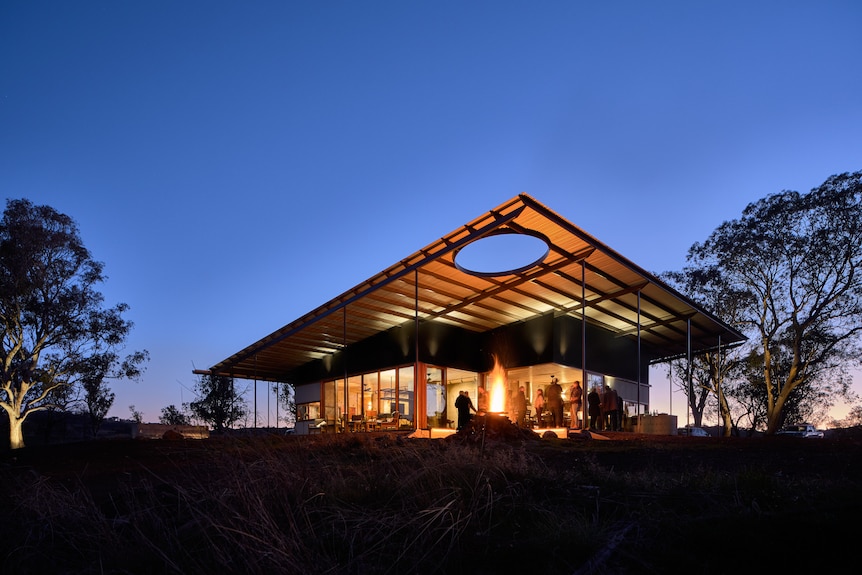 A house with a large room in between trees light up at dusk.